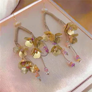 Detalle de pendientes boho de flores doradas con borlas y cuentas de colores