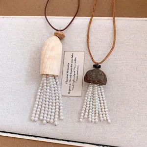 Collier artisanal en bois naturel et coque avec d'élégants glands en perles blanches