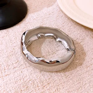 Gros plan d'un bracelet jonc ovale argenté ondulé minimaliste sur tissu crème texturé