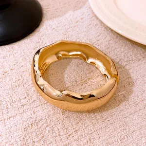 Détail d'un bracelet ovale doré avec un design ondulé unique et une finition brillante
