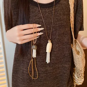 Gros plan détaillé des pendentifs en bois et des pompons en perles de ce collier