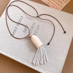 Détail en gros plan du collier avec pendentif en bois et glands en perles blanches