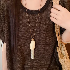 Gros plan d'un collier artisanal en coque de bois et glands de perles sur un pull marron