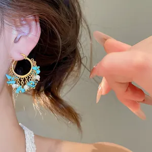 Gros plan de boucles d'oreilles créoles dorées 18k avec pampilles turquoise et perles.
