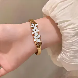 Vue rapprochée d'un bracelet élégant en acier doré avec des fleurs en émail blanc