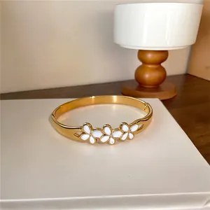Vue rapprochée d'un élégant bracelet en acier doré avec des détails de fleurs en émail blanc
