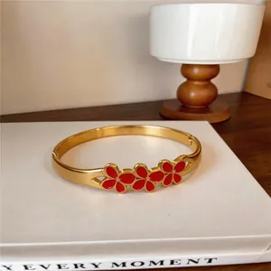 Gros plan d'un bracelet jonc en acier doré orné de trois fleurs en émail rouge.