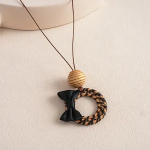 Close-up detail of vintage woven rattan pendant necklace featuring a black bow and wooden bead