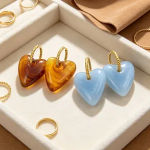 Nahaufnahme von übergroßen Herz-Ohrringen im Retro-Look mit marmoriertem Harzdesign in Gold.
