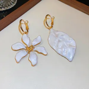 Primer plano de aros dorados asimétricos con flor y hoja de esmalte blanco elegante