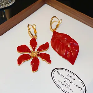Vista detallada de pendientes asimétricos de esmalte rojo con flor y hoja