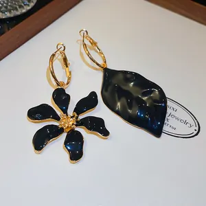 Detalle de pendientes asimétricos negros de flor y hoja con elegante baño de oro.