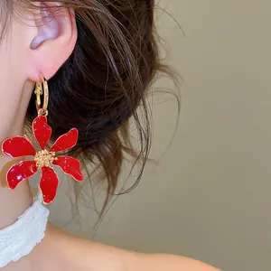 Vista detallada de un elegante pendiente de aro con flor de esmalte rojo en una modelo
