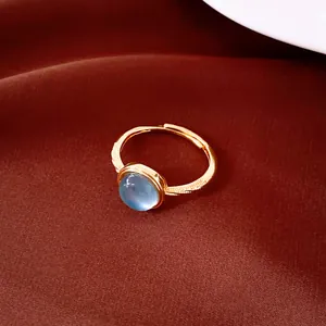 Primer plano de un elegante anillo abierto bañado en oro con una piedra de circón azul