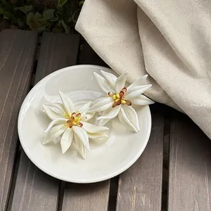 Primer plano de pendientes de flor de acrílico blanco sobre platillo de cerámica blanca.