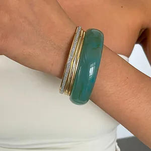 Detailweergave van vintage groene hars en goudkleurige metalen armbanden om een pols