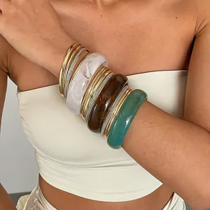 Close-up van gestapelde retro hars en goud metalen armbanden met marmerpatronen op de arm