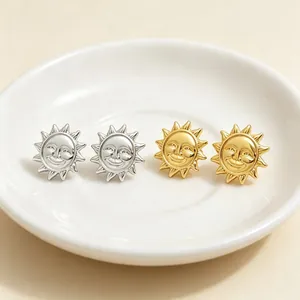 Vue macro de boucles d'oreilles soleil souriant en relief or et argent sur plateau blanc