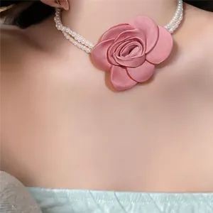 Zoom sur un collier de perles élégant à double rang avec une grande rose en tissu rose.