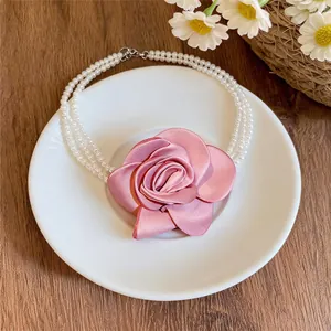 Collier de perles élégant à plusieurs rangs orné d'une grande rose en tissu rose.