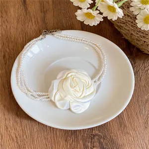 Vue détaillée d'un collier de perles multicouche avec un grand pendentif rose en tissu blanc.