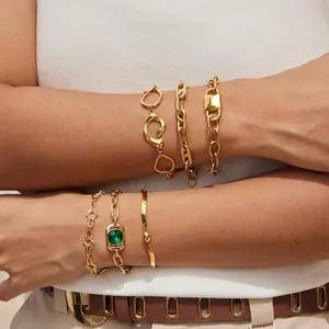 Primer plano de elegantes pulseras de acero inoxidable dorado con dijes y una gemma verde
