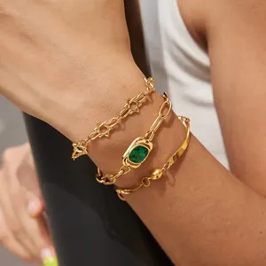 Primer plano de pulseras de acero inoxidable doradas con una piedra preciosa verde ovalada.