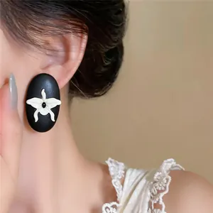 Macro view of black wooden oval stud earrings featuring a white orchid floral design detail