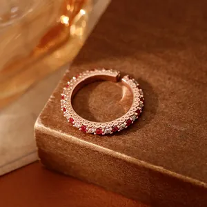 Détail d'une bague ouverte en or rose avec des pierres rouges et blanches sur fond brun