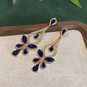 Elegante goldfarbene Hängeohrringe mit tiefblauen Wassertropfensteinen und glitzernden Kristallen.