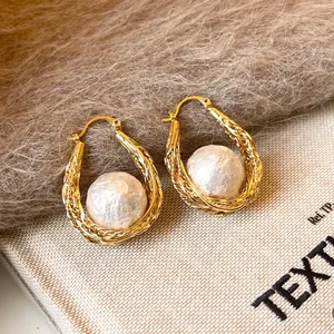 Gros plan de boucles d'oreilles créoles dorées 18 carats avec une perle baroque au centre.