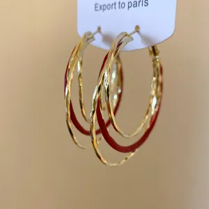 Gros plan de créoles torsadées dorées avec détails en émail rouge sur une carte.
