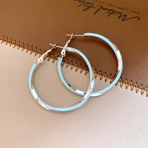 Elégantes créoles torsadées en émail bleu clair sur un fond en cuir marron texturé.