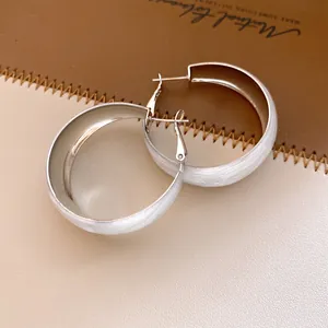 Vue détaillée de boucles d'oreilles créoles en émail blanc sur un fond en cuir raffiné.