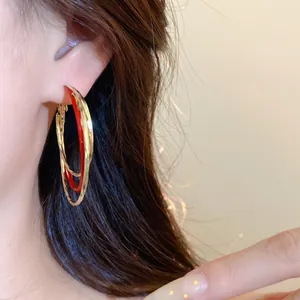 Vue détaillée d'élégantes créoles torsadées en émail rouge et doré portées à l'oreille