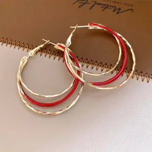 Gros plan détaillé de boucles d'oreilles créoles dorées torsadées avec un émail rouge élégant