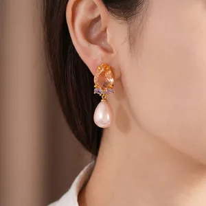 Élégantes boucles d'oreilles dorées avec zircon et perle rose portées par un modèle