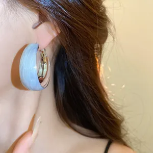 Gros plan d'une boucle d'oreille créole torsadée argentée avec émail marbré bleu sur l'oreille