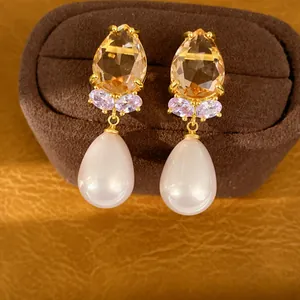 Vue détaillée de boucles d'oreilles dorées avec pierre champagne et perle en forme de poire