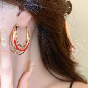 Vue détaillée des boucles d'oreilles créoles torsadées en émail rouge sur l'oreille