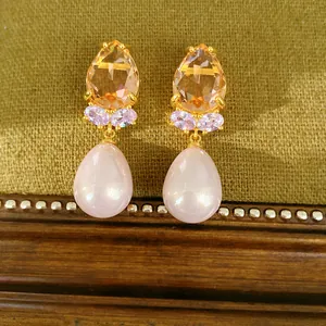 Gros plan de boucles d'oreilles dorées avec zircon champagne et perles roses en goutte.