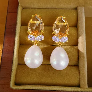 Gros plan d'élégantes boucles d'oreilles goutte dorées avec zircon champagne et perle