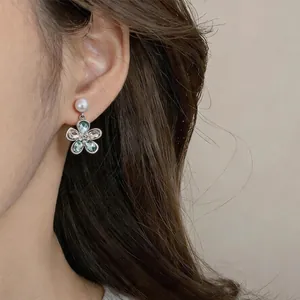 Nahaufnahme von eleganten silbernen Blumenohrringen mit Kristallen und Perle am Ohr