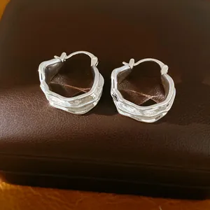 Detalle de pendientes de aro plateados con diseño plisado sobre estuche de cuero marrón.