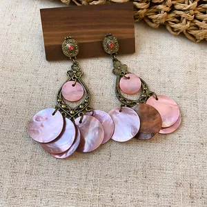 Close-up of bohemian bronze earrings with pink shell discs and red rhinestones