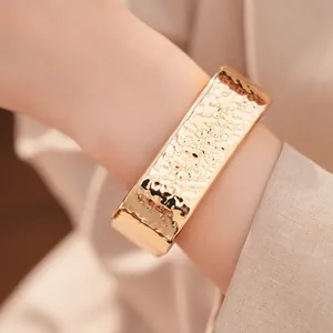 Primer plano de un brazalete ancho de oro martillado con textura de pliegues en la muñeca