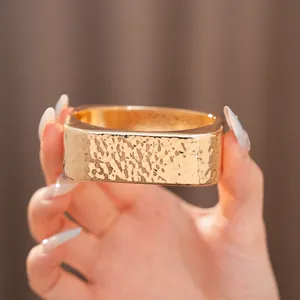 Primer plano de un brazalete rectangular de oro martillado con acabado metálico texturizado