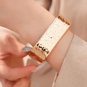 Primer plano detallado de un brazalete rectangular de oro martillado con textura plisada