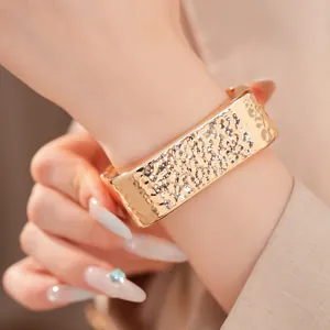 Detalle de una pulsera rígida rectangular dorada con un elegante acabado martillado