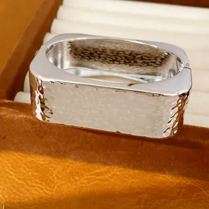 Primer plano de brazalete rectangular plateado con textura martillada y brillo metal